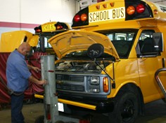 A mechanic works on a yellow school bus in a garage 